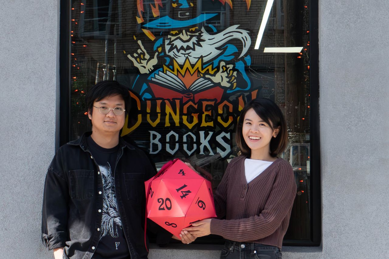 Panat and Carrie holding a giant d20 in front of the Dungeon Books storefront